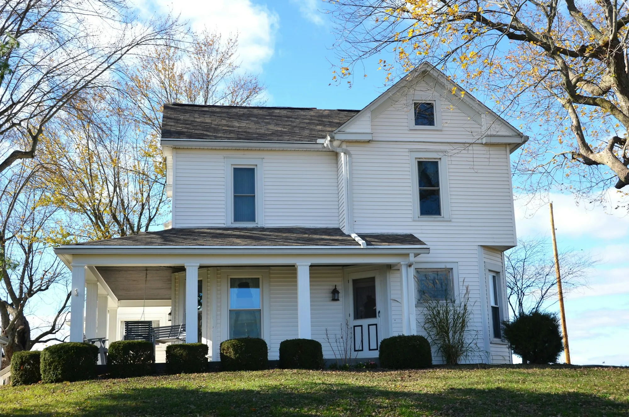 White two-story farmhouse with a gray shingle roof and covered porch