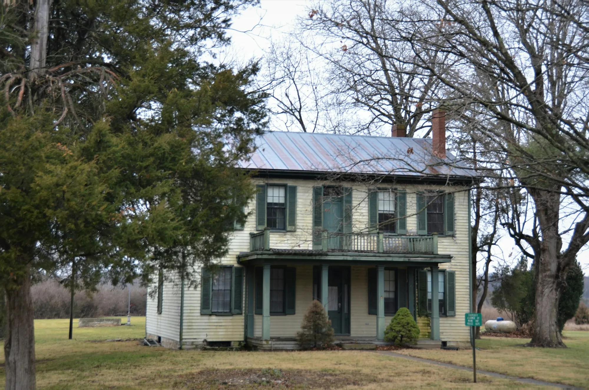 Old two-story farmhouse with a metal roof and bare trees