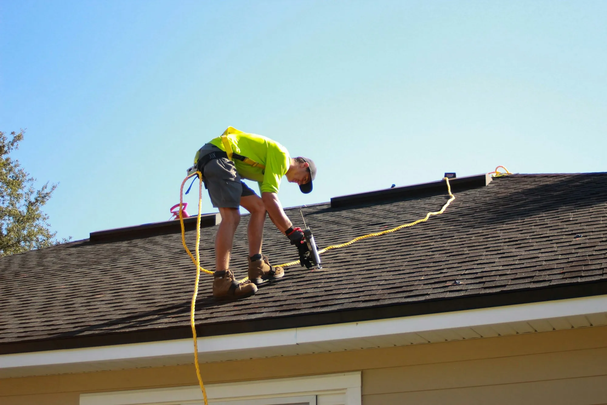 Roofer tied off with a safety rope working near the edge of a shingle roof